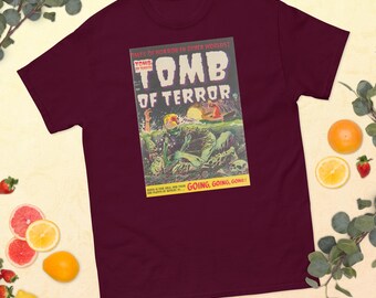 May include: A maroon t-shirt with a vintage comic book cover design. The cover features a monster emerging from water with the text "Tomb of Terror" and "Going, Going, Gone!"