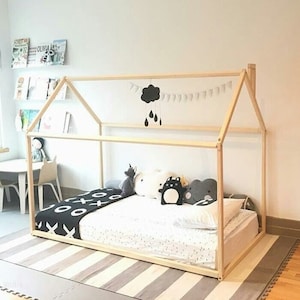 May include: A wooden house-shaped bed frame with a white mattress and black and white patterned bedding. The bed is decorated with stuffed animals and a cloud-shaped mobile with raindrops.