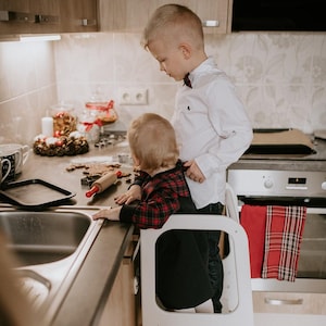 Two young kids using a matte black child step stool near the kitchen sink, helping parents teach independent handwashing habits.