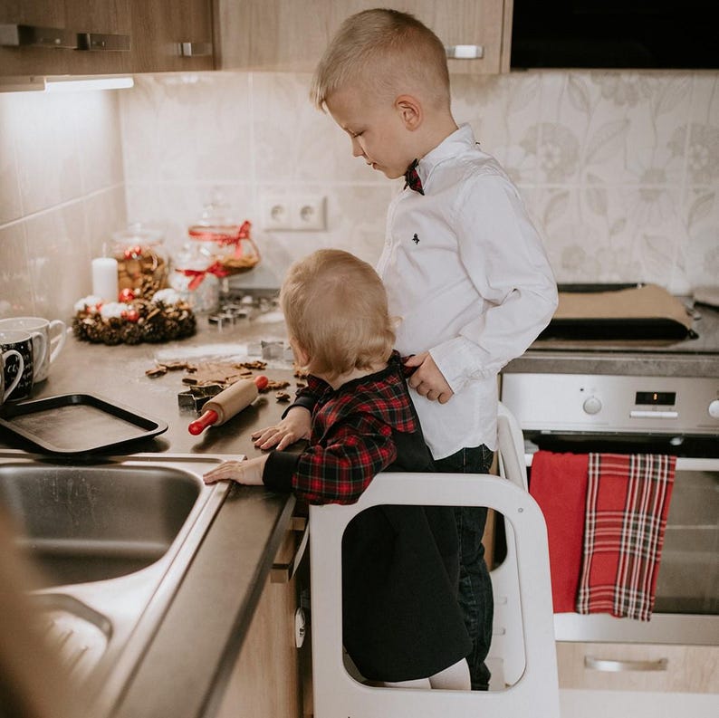 Two young kids using a matte black child step stool near the kitchen sink, helping parents teach independent handwashing habits.
