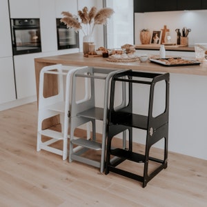 May include: Three wooden step stools in white, gray, and black. The stools have two steps and a safety rail. They are designed to help children reach higher surfaces.