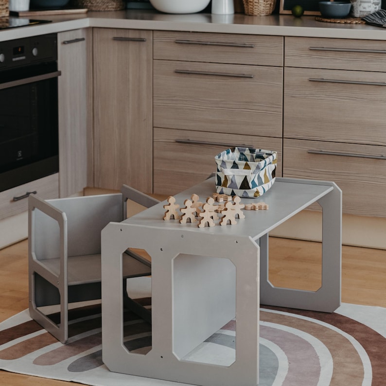Grey toddler weaning table and chairs arranged on a patterned rug near the kitchen.