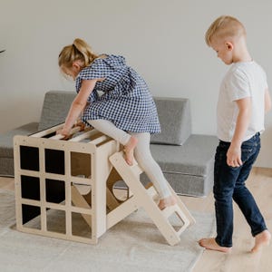 Two toddlers actively playing and climbing on a indoor activity cube with a ramp attachment.