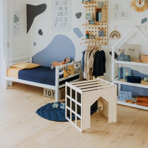 Convertible play cube placed near a bed frame, acting as an indoor climbing structure.