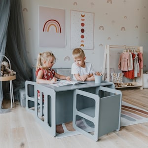 Two young toddlers reading together at a grey activity table in a nursery.