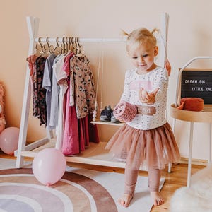 Little girl in a festive dress playing beside a white clothing stand, offering charming inspiration for a toddler room birthday makeover.