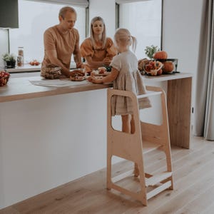 Natural wood look montessori standing tower surrounded by family at the island, creating a warm bonding experience during Thanksgiving prep.