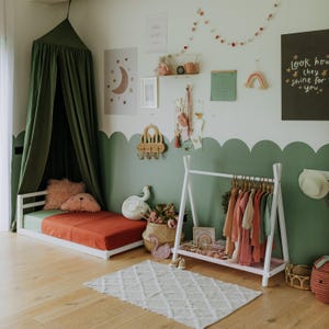 White wooden clothes rack arranged in a sage green nursery, offering a practical Thanksgiving gift for parents organizing child outerwear.