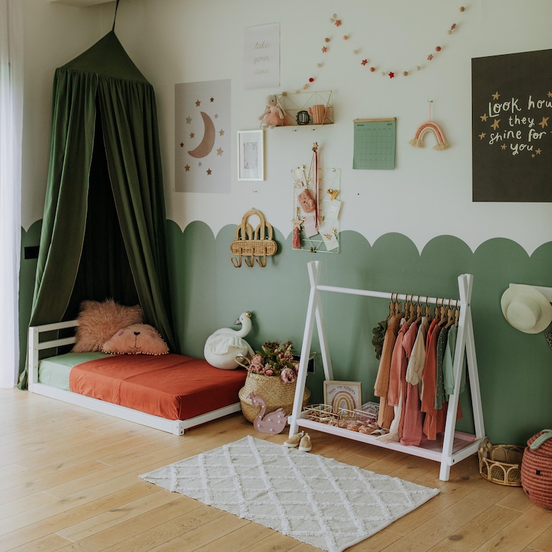 White wooden clothes rack arranged in a sage green nursery, offering a practical Thanksgiving gift for parents organizing child outerwear.