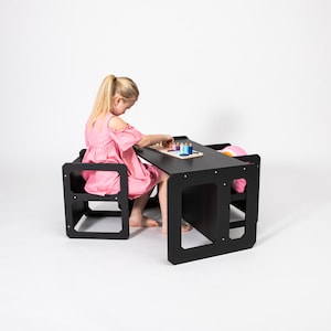 A young girl crafting with art supplies at a black compact toddler table with cube seats in a studio setting.