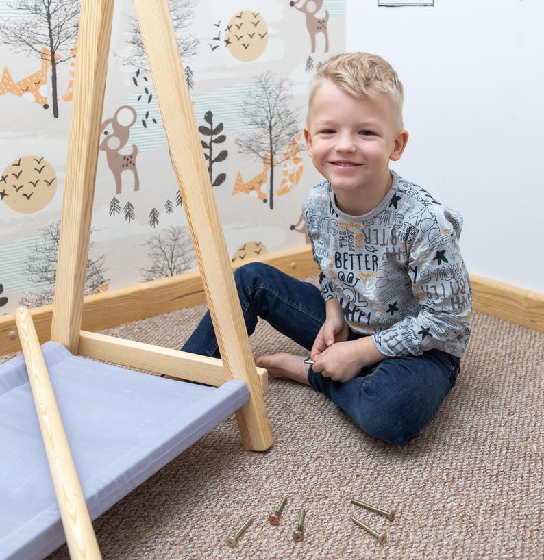 Young boy resting beside timber wardrobe components during setup, demonstrating a simple assembly process for foster parents.