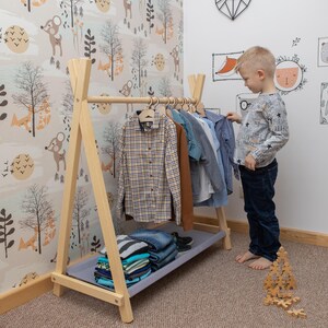 Young boy picking out a shirt from an open timber rack, helping parents foster self-dressing habits before the first day of preschool.