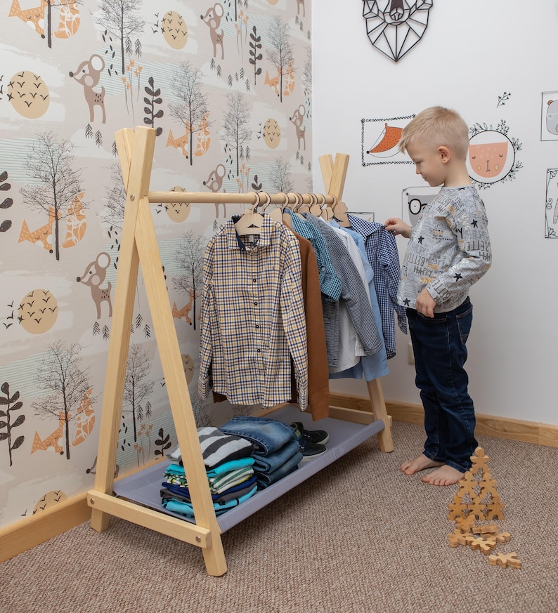 Young boy picking out a shirt from an open timber rack, helping parents foster self-dressing habits before the first day of preschool.