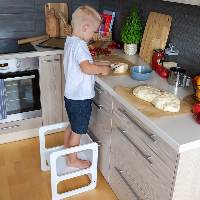 Boy helping with cooking while standing on a white convertible step stool in the kitchen.