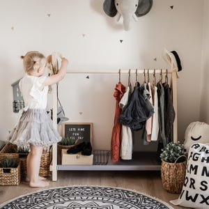 Little girl choosing dresses from a low birch rack, helping foster independent dressing habits in young children before kindergarten.