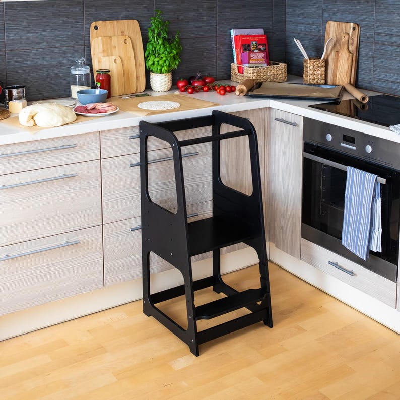 Black child standing stool set near a modern counter, offering sleek organization for child-friendly kitchen spaces.