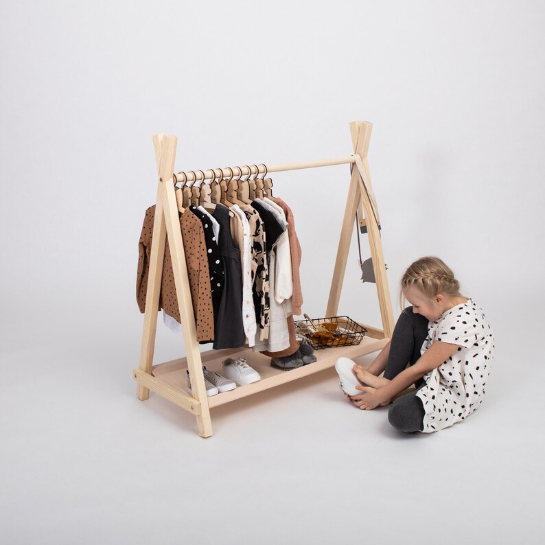 Little girl putting on shoes near an open birch wardrobe rack, helping moms teach kids independence during morning routines.