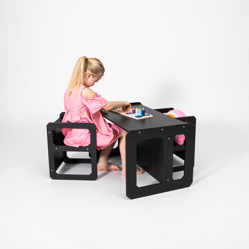 Young girl crafting at a black painted toddler weaning table and chair set in a studio shot.