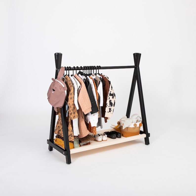 Black wooden clothing rack with a beige fabric shelf, serving as a charming baptism gift for parents setting up a girl nursery.