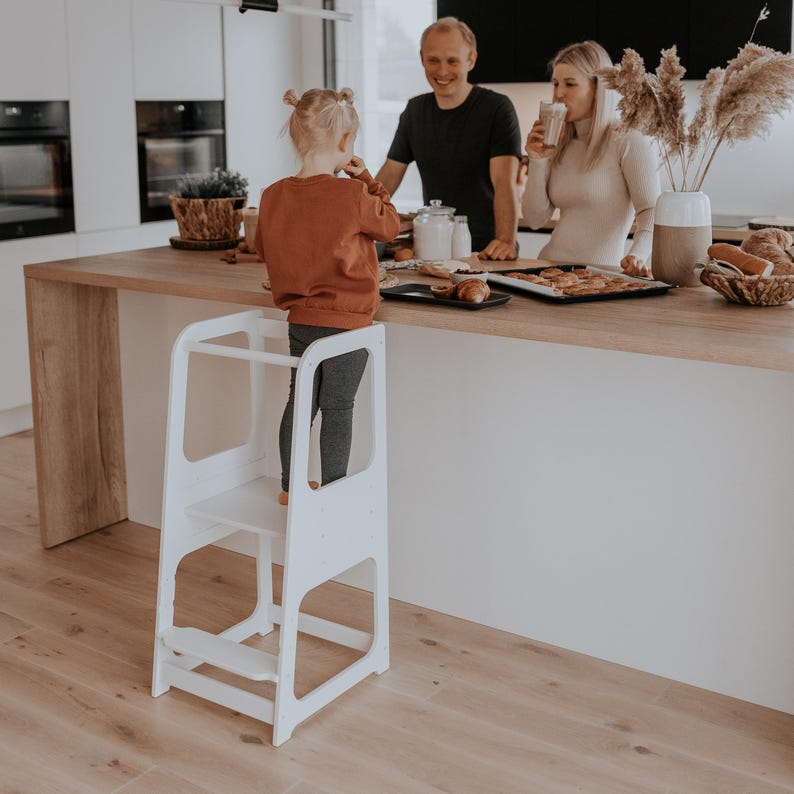 White toddler step stool placed by a sunlit kitchen island, giving godmothers and aunts a thoughtful housewarming gift idea.