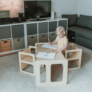 A toddler drawing with crayons at a natural birch plywood play desk near living room storage shelving.