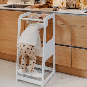 Little girl in patterned leggings climbing up a white toddler step stool, solving daily morning routine chaos for busy families.
