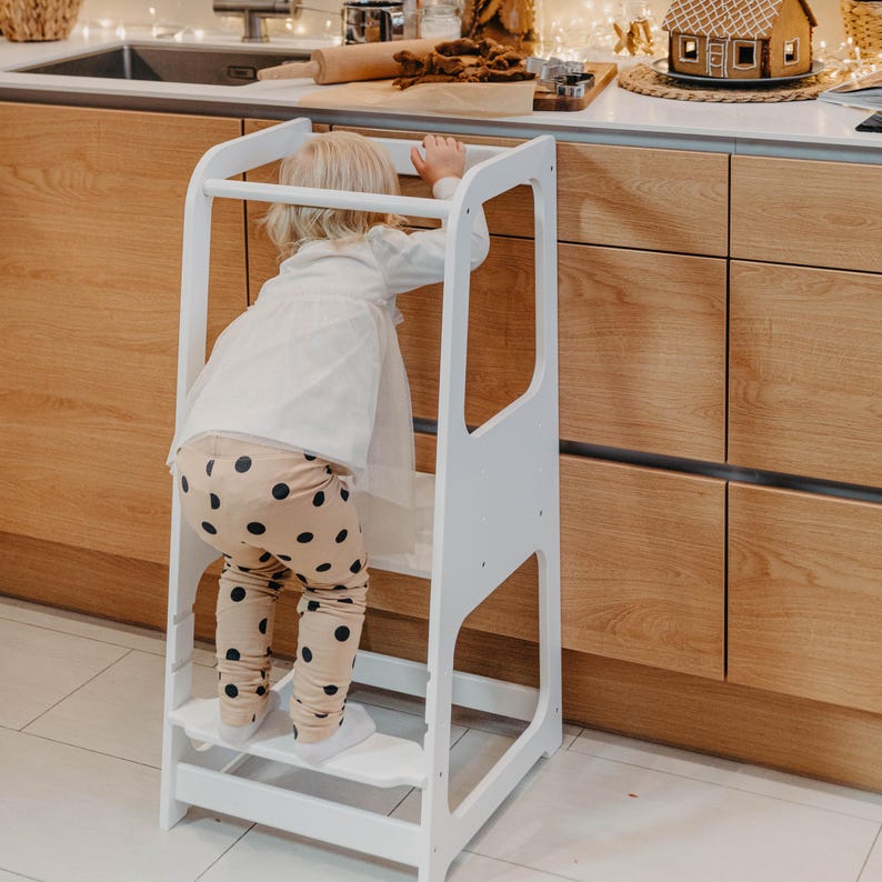 Little girl in patterned leggings climbing up a white toddler step stool, solving daily morning routine chaos for busy families.