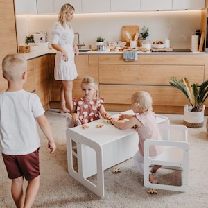 Two toddlers sitting and eating at a white weaning table in the kitchen area.
