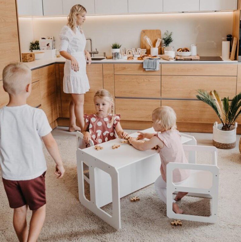 Two toddlers sitting and eating at a white weaning table in the kitchen area.