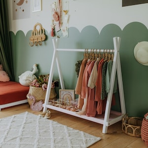 White timber open wardrobe stand in a sage green nursery corner, offering a practical housewarming gift idea for young families.