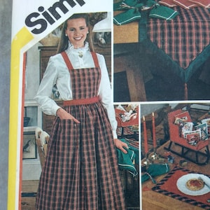 May include: A red and black plaid apron with a ruffled hem and red straps. The apron is worn over a white blouse with a lace collar. The text "BONUS - Pattern includes special chart on how to work with plaids. Blouse not included" is at the bottom of the image.