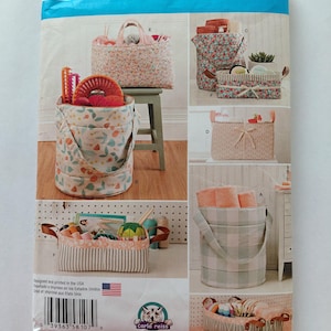 May include: A Simplicity sewing pattern envelope 8107 for fabric storage baskets and bins. The front displays various designs including round and rectangular containers with floral, plaid, and solid fabrics, featuring handles and ribbons.