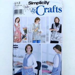 May include: A Simplicity Crafts sewing pattern envelope, number 8313, featuring illustrations of four variations of a sleeveless apron with pockets. The front displays the brand name, a barcode, and size range S, M, L, XL for the garment designs.