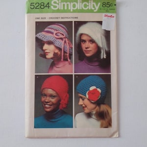 May include: Vintage Simplicity crochet pattern 5284 featuring four different hat designs. The hats include a sun hat, a fuzzy hat with fringe, a red beanie, and a blue hat with a flower. The pattern is marked "One Size - Crochet Instructions."