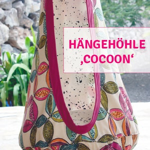 May include: A fabric cocoon-shaped hanging chair with a floral pattern in pink, orange, and teal on a cream background. The chair has a magenta trim and handle. The text "HÄNGEHÖHLE, COCOON" is visible.
