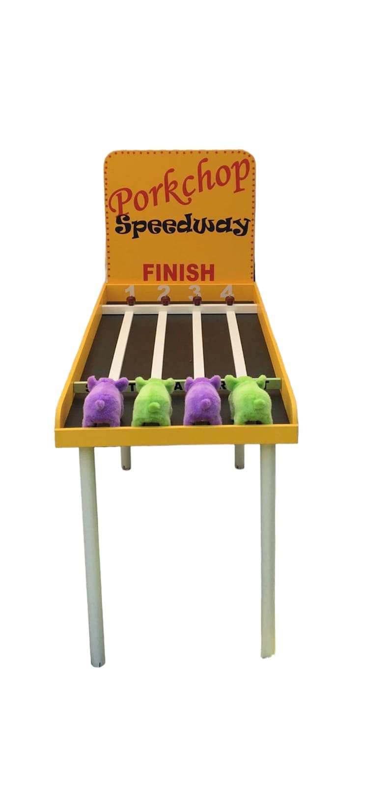 以下が含まれることがあります： 「Porkchop Speedway」と「Finish」の文字が書かれた黄色とオレンジのウッド製の豚レースゲーム。4匹のぬいぐるみ豚がスタートラインに並んでいます。