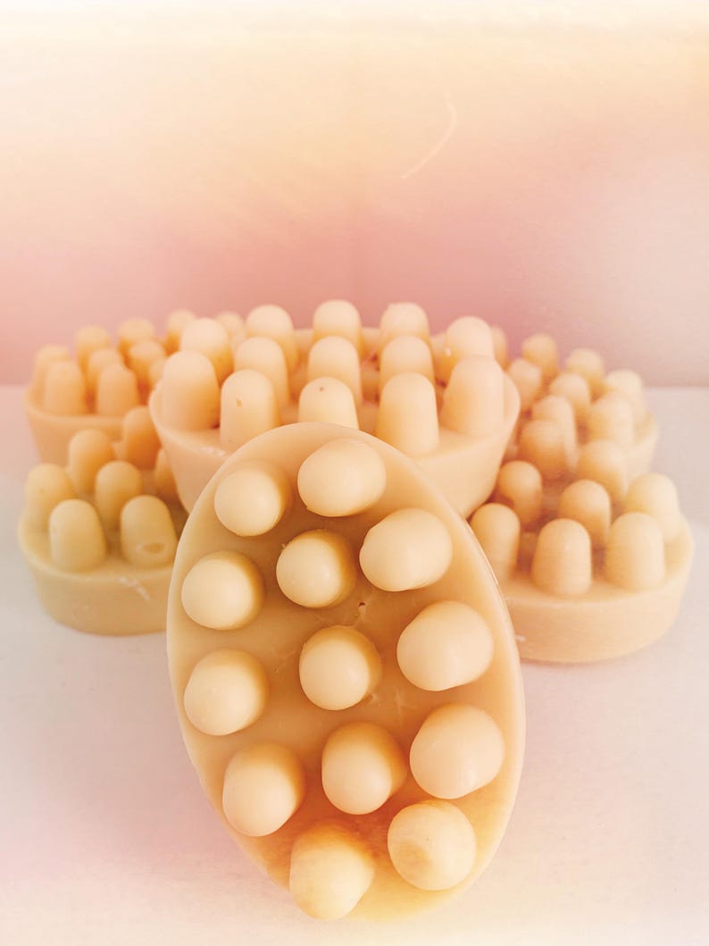 Pu&ograve; includere: Primo piano di una saponetta rotonda di colore beige con una superficie testurizzata. Il sapone ha un motivo di piccoli rilievi. Ci sono diverse altre saponette sullo sfondo.
