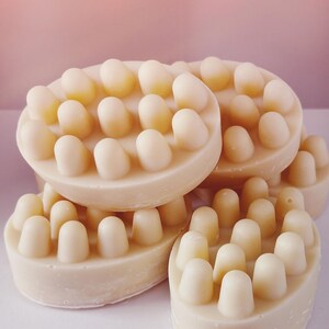 Pu&ograve; includere: Primo piano di quattro saponette da bagno color avorio con protuberanze rialzate sulla superficie. Le saponette sono impilate l'una sull'altra.