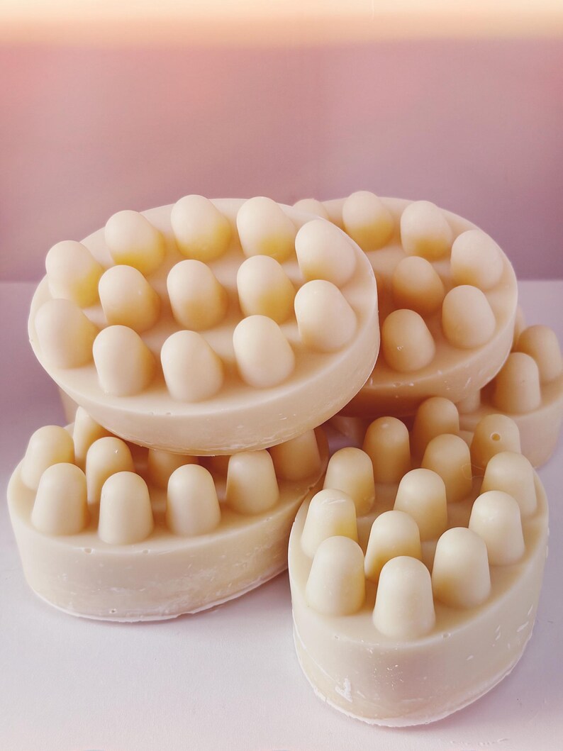 Pu&ograve; includere: Primo piano di quattro saponette da bagno color avorio con protuberanze rialzate sulla superficie. Le saponette sono impilate l'una sull'altra.