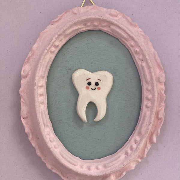 Keramische tand. Schattige kawaii keramische tandminiatuur in een ovale lijst, met houten achtergrond.