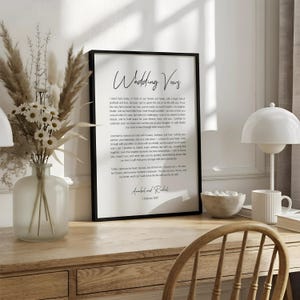 a framed quote on a white desk, surrounded by various objects such as a notebook, a cup, and a vase with dried flowers.
