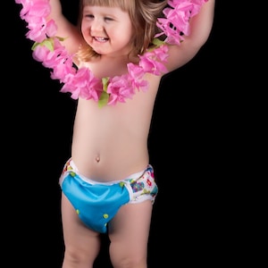 May include: A young child wearing a blue and white patterned nappy cover with a pink flower lei around their neck. The child is smiling and holding the lei in their hands.
