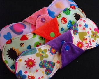 Puede incluir: Cuatro compresas menstruales de tela reutilizables con diferentes patrones y diseños coloridos. Las compresas tienen broches y están hechas de tela suave.