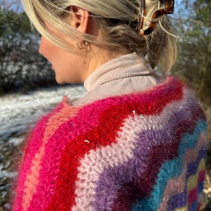 May include: A colourful, fuzzy, striped sweater with a rainbow pattern. The sweater is made of a soft, fluffy yarn and has a relaxed fit.