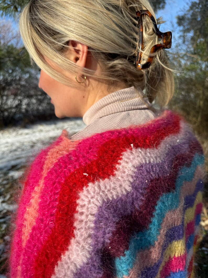 May include: A colourful, fuzzy, striped sweater with a rainbow pattern. The sweater is made of a soft, fluffy yarn and has a relaxed fit.