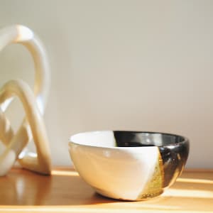 May include: A white and black ceramic bowl with a gold stripe. The bowl is sitting on a wooden surface.