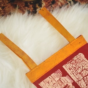 May include: A red felt pennant with a map design in white, featuring a yellow border and two yellow straps. The pennant is likely a souvenir or decorative item.
