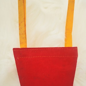 May include: A red felt pennant with two yellow straps. The pennant has a rectangular shape with a stitched seam along the top. The yellow straps are attached to the top of the pennant.