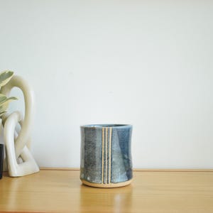 May include: A blue ceramic mug with a light blue and white stripe design. The mug is sitting on a wooden surface.