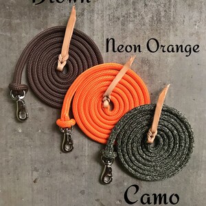 May include: Three coiled dog leads in brown, neon orange, and camouflage. The leads have a leather handle and a silver clip.